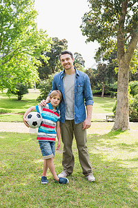 父亲和儿子带着球在公园微笑图片