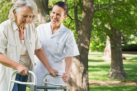 帮助成年妇女的妇女 在公园用步行车成人树木照顾者损伤残疾人老化斗争草地退休身体图片