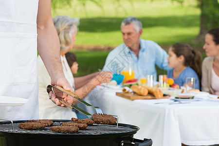 与大家庭在公园吃午餐的烧烤炉男性烹饪草地团结父母兄弟姐妹祖父花园家庭男人图片
