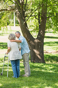 成年男子在公园用步行器协助妇女闲暇成人病人照顾者帮助树木友谊残障机动性疾病图片