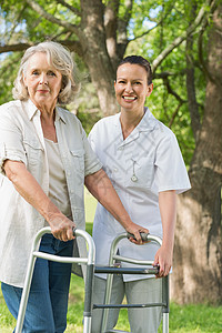 帮助成年妇女的妇女 在公园用步行车草地老年人士照顾者斗争机动性损伤树木母亲残疾人图片