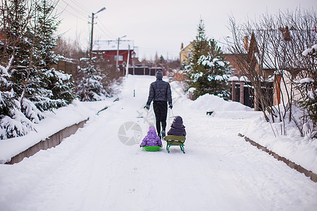 年轻父亲在雪地外的雪橇上滚动着他可爱的小女儿图片