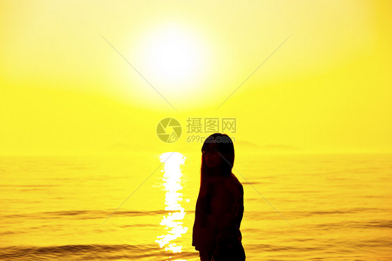 年轻女子站在日落光下沙滩上图片