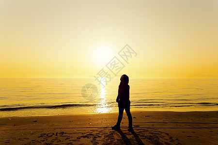 青春女性站在日落的海滩上图片