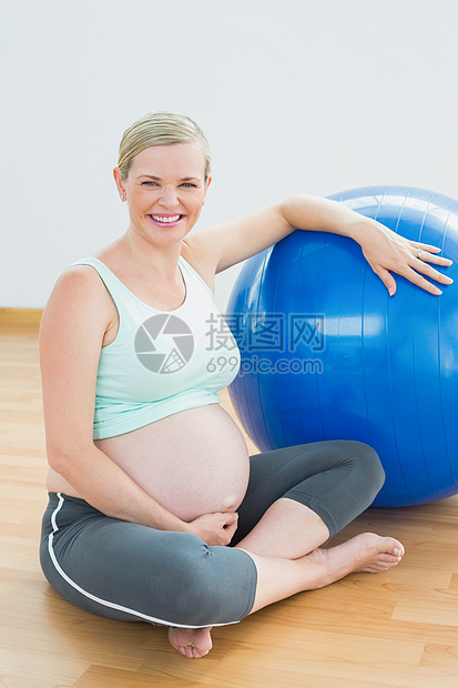 坐在健身球旁边的孕妇在镜头上微笑着微笑男性健身房孕妇装男人怀孕闲暇运动服运动瑜伽护理图片