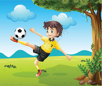 一个男孩在大树附近的山上踢足球图片