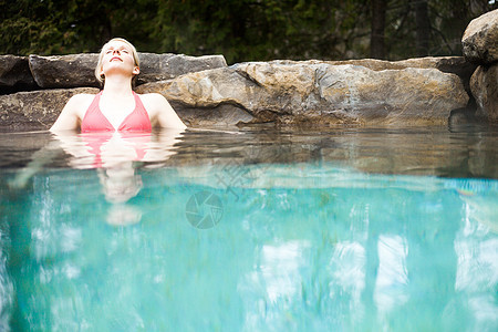 在北欧斯帕放松的年轻女性金发女郎旅行游客森林女士比基尼享受水疗温泉岩石图片