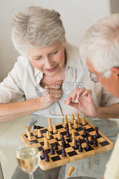 玩象棋和喝白酒的老夫妇微笑棋盘快乐酒精男性住所酒杯老年退休家庭厨房图片