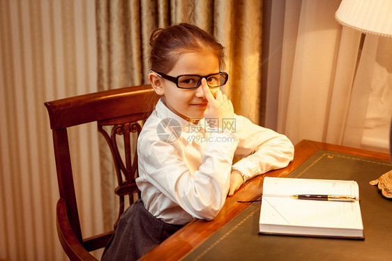 坐在桌子后面的眼镜上的女孩图片