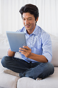 用平板电脑坐在沙发上的快乐男人住所滚动客厅家庭家庭生活公寓触摸屏闲暇微笑药片图片