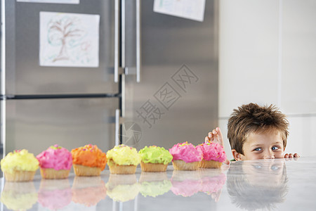 小男孩在厨房的一排纸杯蛋糕柜台顶峰图片