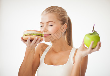 女人闻到汉堡和拿着苹果伤害营养芝士食物垃圾包子肥胖脂肪水果保健图片