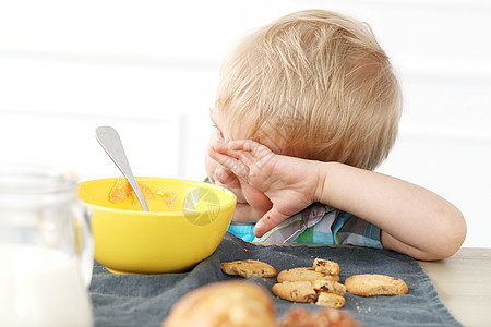 坐在桌边的年轻男孩眼睛金发女郎桌子蓝色孩子食物衬衫公寓房子早餐图片