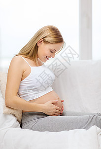 快乐的孕妇抚摸她的肚子沙发幸福母性婴儿父母家庭女孩男生女士女性图片