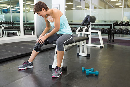坐在脚膝受伤的长凳上女性运动服女士调子运动支撑闲暇健身室身体护理图片