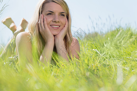 躺在草地上微笑着笑着的 穿着日光浴衣的金发美女图片