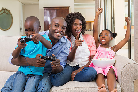 在沙发上玩电子游戏的快乐家庭放松爆米花游戏女士女孩女性住所欢呼微笑儿子控制器图片