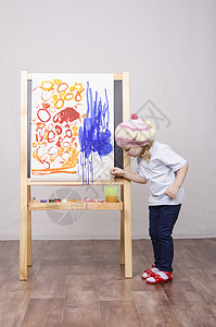 女孩画女孩艺术家在画布上的油漆孩子乐趣微笑蓝色眼睛童年绘画画架平局笑声背景