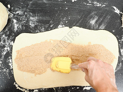 人将肉桂混合与烟灰缸混在一起的肉桂传播到一个平坦的杜格上桌子烹饪床单糕点包子美食面团工作甜点面粉图片