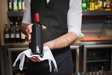 拿着一瓶红酒的英俊服务员酒精酒吧微笑夜生活男人职员瓶子衬衫套装马甲背景图片