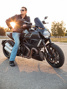 骑自行车的人穿着皮夹克 坐在他的摩托车上运输冒险街道驾驶男性旅行自由日落男人引擎图片