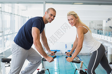 在健身房运动自行车上工作的一对微笑的情侣的侧面视图图片