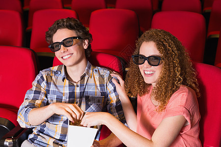 电影放映年轻夫妇在看一部3D电影零食电影院爆米花红色椅子女士活动快乐礼堂男性背景