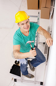 男人在头盔中微笑 在墙上钉钉钉锤子装修指甲公寓梯子技术员工作房子安全帽建筑学图片