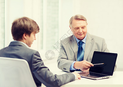 带膝上型计算机的老年男子和青年男子伙伴合伙人士生意人展示广告电脑同事笔记本场景图片