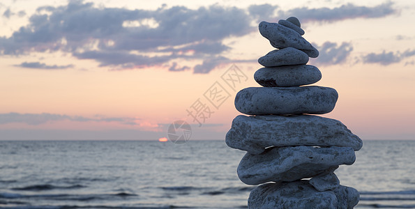 岩石在彼此间沉积支撑太阳日落鹅卵石天空海洋石头图片