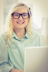 在笔记本电脑上工作的戴眼镜的微笑女商务人士的肖像图片