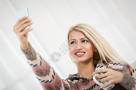 美丽的女孩自取自我水平女子杯子自拍乐趣微笑幸福手机金发女郎图片