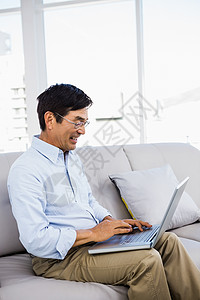 家里的笑人坐在沙发上住所技术公寓长椅男性眼镜衬衫微笑笔记本家庭背景图片