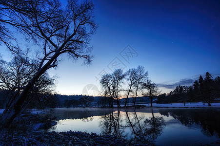 冬季河边的晚夜薄雾日落蓝色森林白色季节树木场景反射天空图片