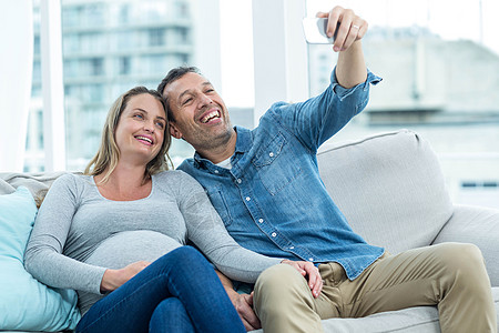 情侣在智能手机上自拍喜悦休闲女性恋人分娩公寓快乐怀孕家庭沙发背景图片