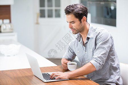 年轻人在笔记本电脑工作时拿着咖啡杯图片