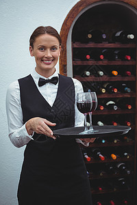 带着红酒杯托盘的微笑女服务员快乐商务酒店午餐服务桌子衬衫马甲人士女士图片