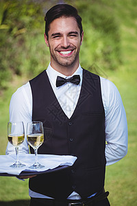 英俊的侍应生拿着两杯红酒的托盘围裙服务员服务衬衫酒精马甲领结奢华餐厅男性图片