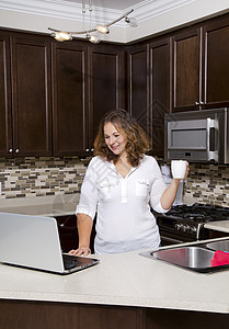 厨房里的女人互联网享受咖啡女性网络技术杯子台面电脑冲浪图片