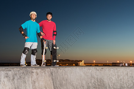 站在混凝土池旁的两名滑板运动员图片