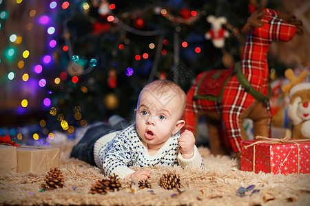 小男孩躺在房间里肚子上 带着圣诞装饰品躺在房间里驯鹿花环快乐玩具惊喜礼物新年说谎盒子毛衣图片