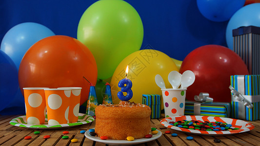 在土气木桌上的生日蛋糕有五颜六色的气球 礼物 塑料杯子和塑料盘子的背景有糖果和蓝色墙壁的在背景中庆典塑料板朋友们蛋糕孩子们蜡烛生图片