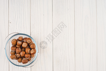 在旧木制桌子上的玻璃碗里的黑桃子水平白色小吃核心营养坚果食物榛子图片