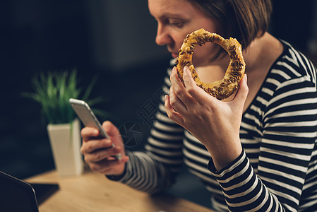 妇女吃芝麻面包圈并使用移动电话背景图片