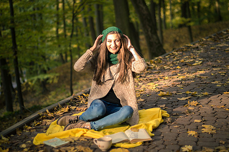 秋天背景坐在赛道上的女孩小路森林公园咖啡蓝色牛仔裤杯子女性快乐成人背景