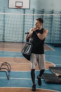 年轻运动员带着运动瓶子和袋子在健身房看远男人中心沉思成人活动水壶运动装体育背景图片