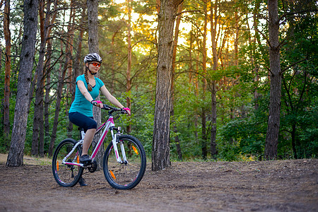 年轻女子在美丽的仙子松林的轨迹上骑着自行车 冒险和旅行概念女性行动运动射线女士耐力头盔活动娱乐运动员图片