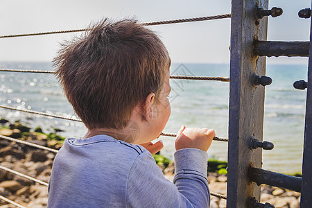 年轻男孩从金属围栏后面向远处的地平线看监狱青年希望男性孩子男生小男孩白色童年海洋图片