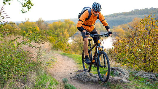 在秋天落岩轨上骑着山车的橙色自行车赛员 极端运动和概念头盔山地车男人娱乐活动岩石冒险行动爬坡橙子图片