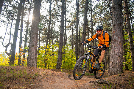 橙色骑着山上摩托机的赛车 中的 自行车名人 在美丽的松树森林里旅行踪迹耐力骑士耐力赛射线车轮头盔速度活动图片